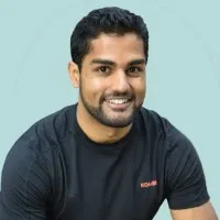 Portrait de Clint Deygoo sur fond bleu ciel, porte un t-shirt gris foncé avec une écriture rouge sur le côté gauche